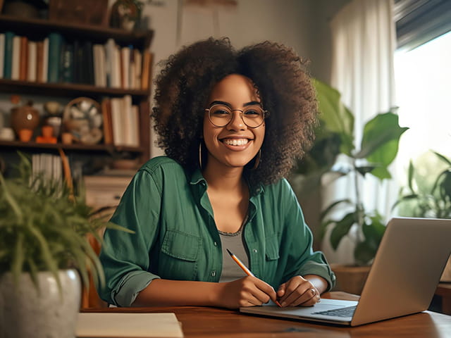 Jovem negra sorrindo enquanto escreve e usa notebook